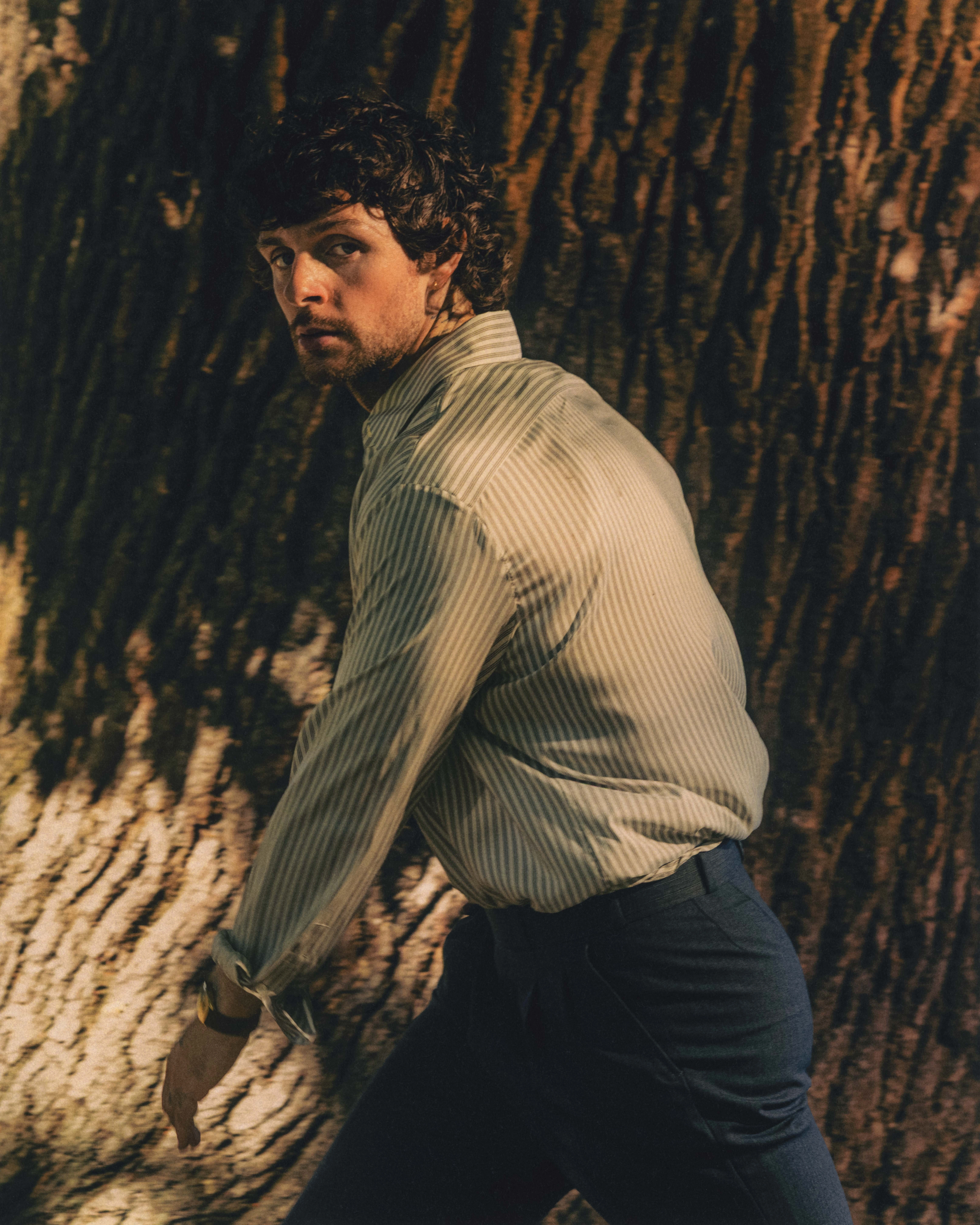 Tom Grennan w pasiastej koszuli w scenerii leśnej – fotografia prasowa singla Wrapped In Gold