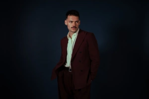 James Marriott w bordowym garniturze na ciemnym tle – zdjęcie promujące singiel Lovestruck i album Warning Signs, fot. Sam McMahon