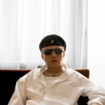 Kajetan Wolas w białej koszuli, czarnym berecie i okularach przeciwsłonecznych – archiwalna fotografia promocyjna Sony Music