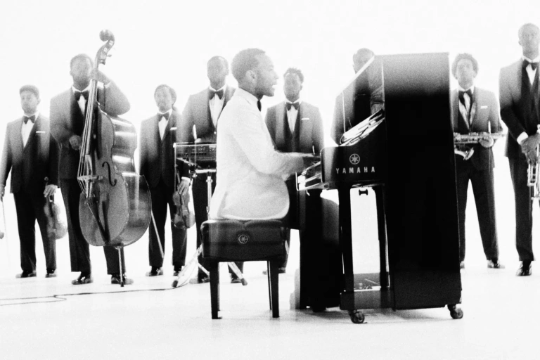John Legend gra na fortepianie w otoczeniu muzyków w czarnych garniturach – album Muse 2026